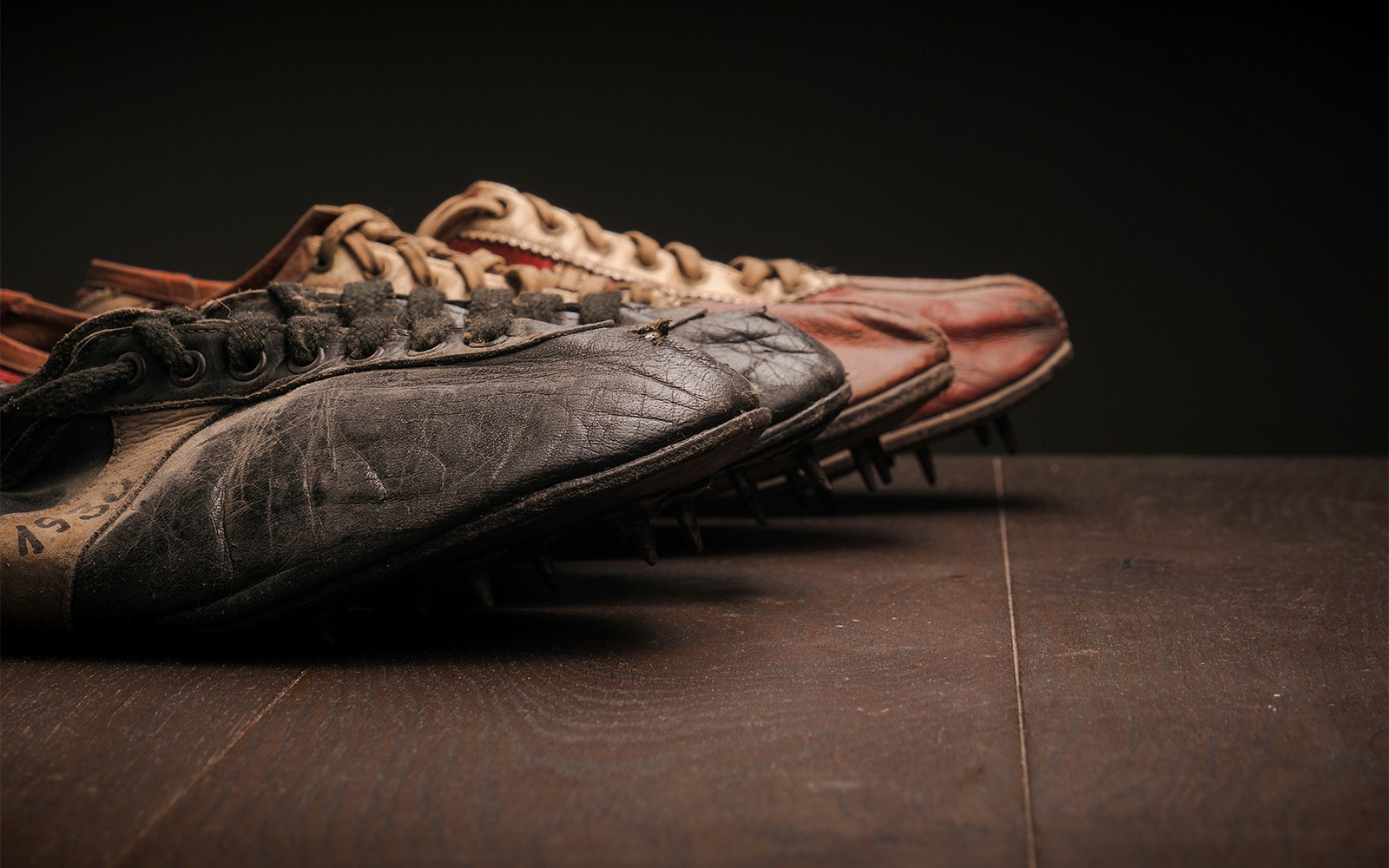 Vintage football boots with worn leather and metal studs on a wooden surface.
