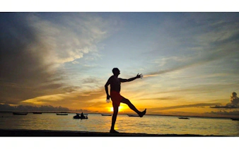 Silhouette of a person on a Zanzibar beach at sunset, with boats in the background.