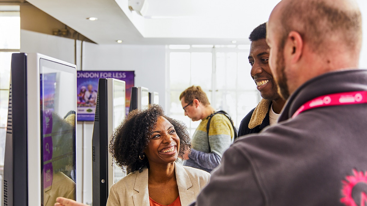 Guide assisting tourists with London Eye tickets at kiosk.