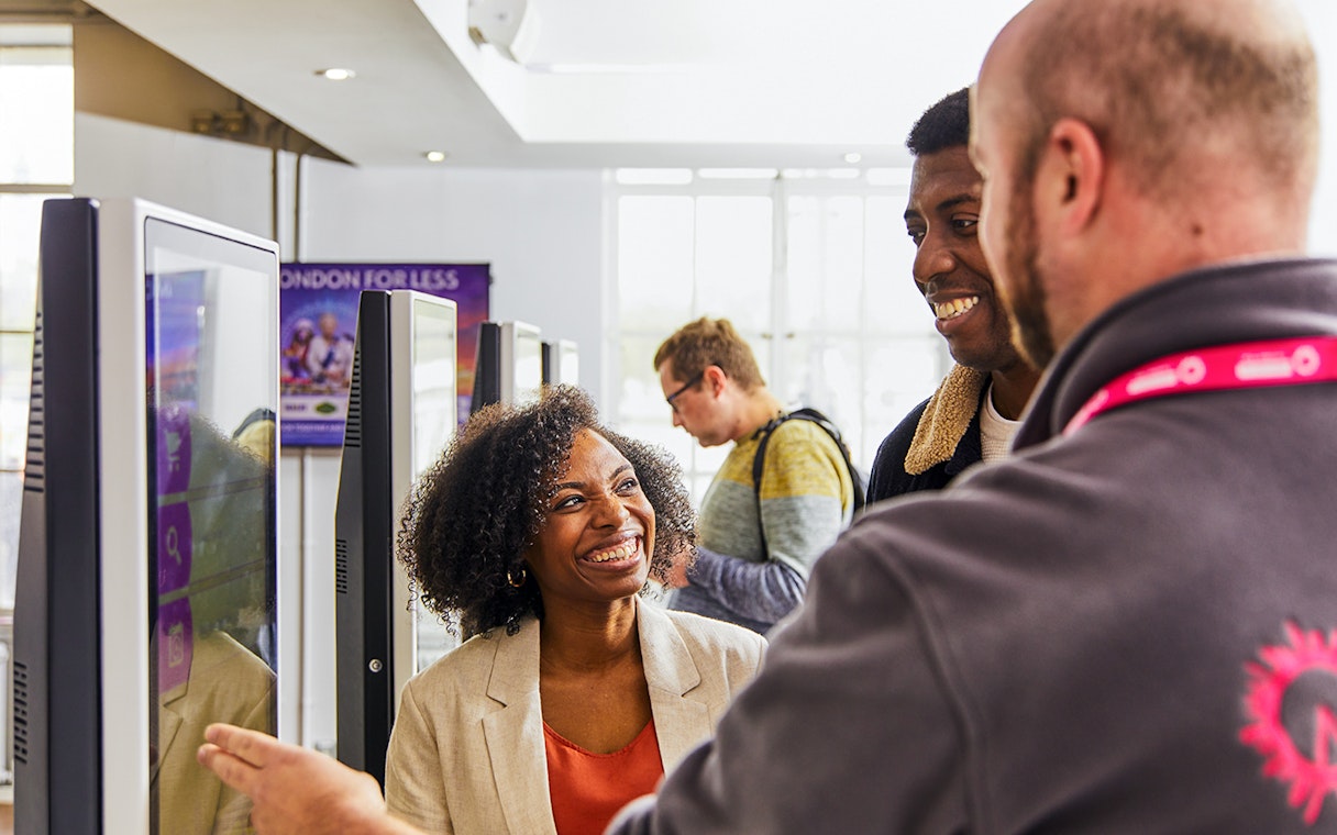 Guide assisting tourists with London Eye tickets at kiosk.