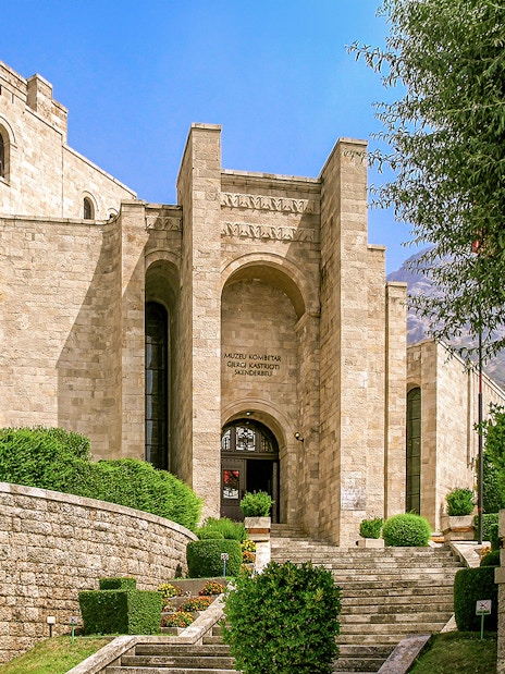 Skanderbeg Museum entrance at Kruje Castle, Albania, with stone architecture and surrounding greenery.