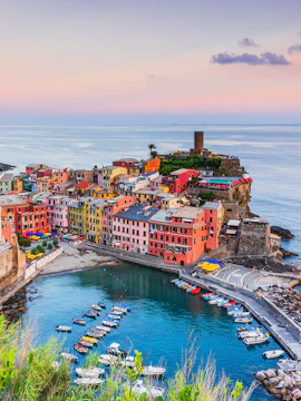 Colorful buildings and boats in Vernazza, Cinque Terre, viewed from a hill at sunset, near La Spezia.