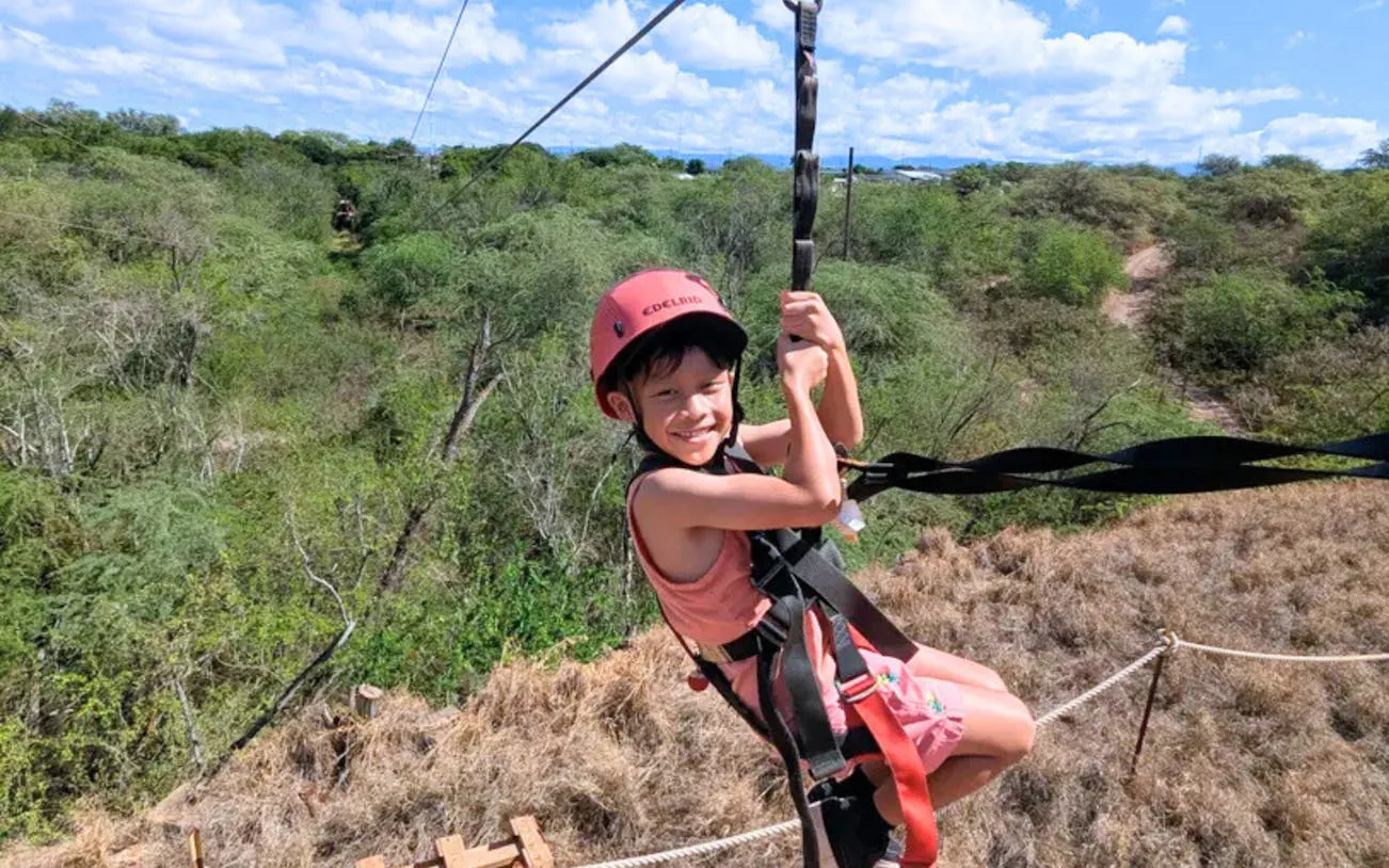 Child enjoying zipline adventure over lush landscape with modern braking system.