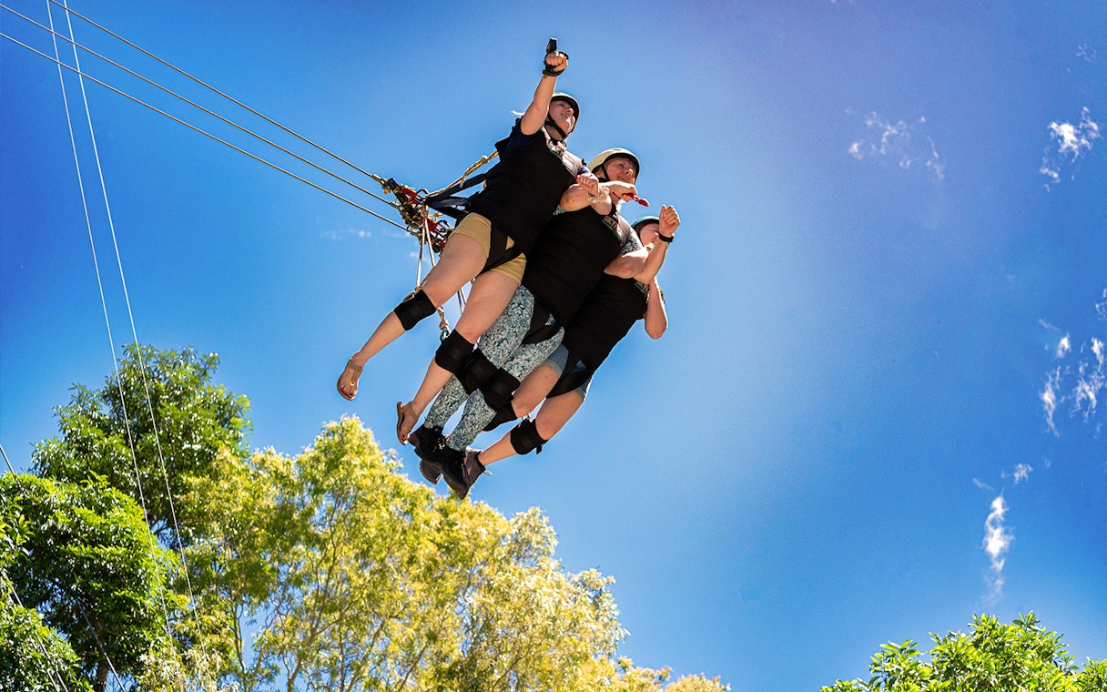 Three people on the Cairns Giant Swing against a clear blue sky.