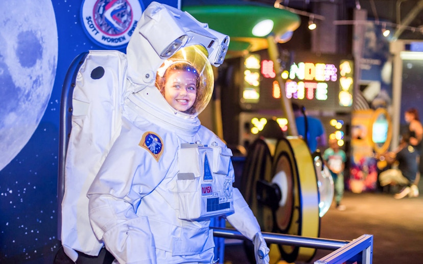 Child in astronaut suit at WonderWorks exhibit with space-themed background.