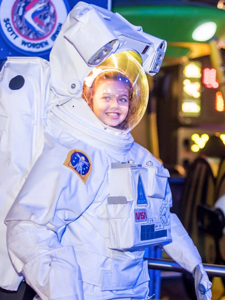 Child in astronaut suit at WonderWorks exhibit with space-themed background.