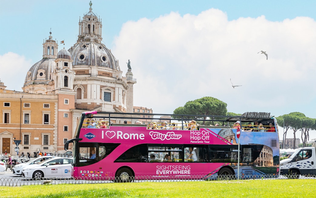 Open-top tour bus in Rome near historical architecture.