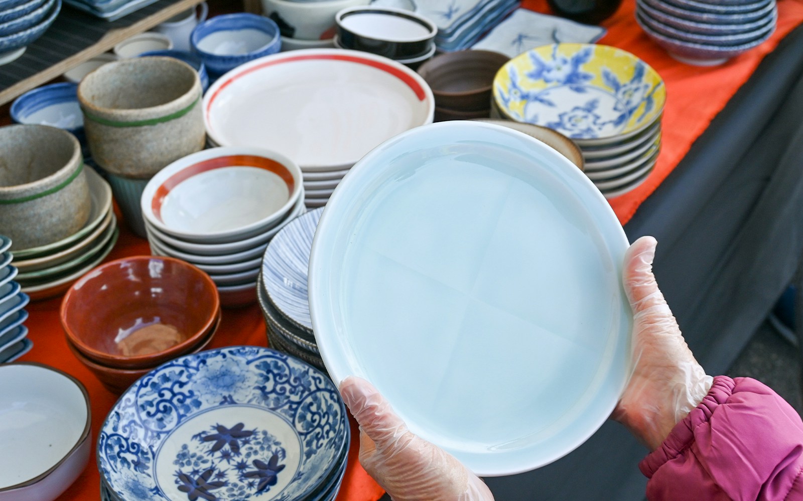 Hands holding a ceramic plate at a pottery market in Japan.