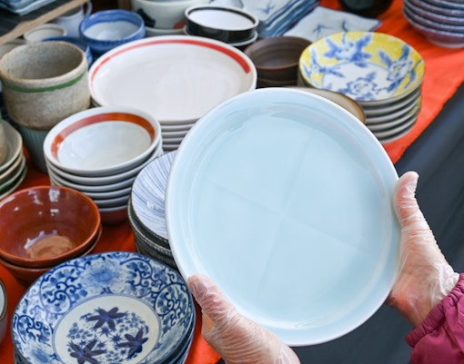 Hands holding a ceramic plate at a pottery market in Japan.