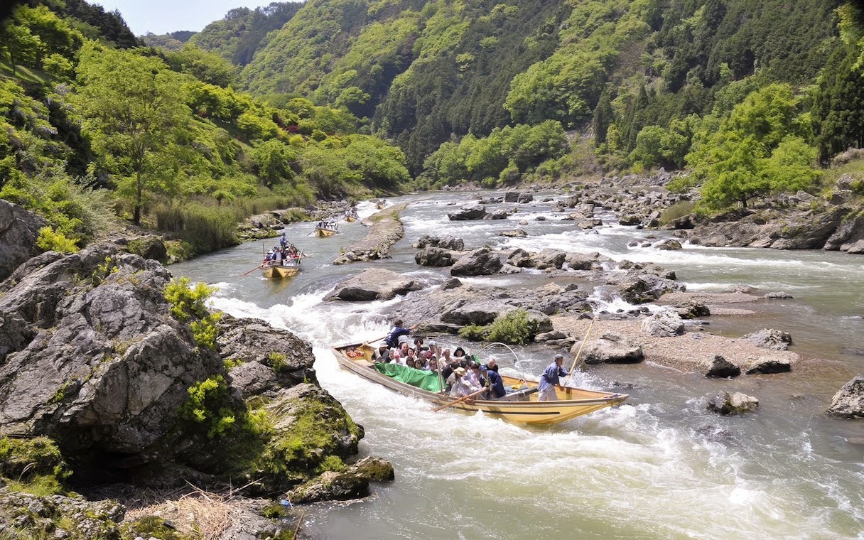Boat ride on Hozugawa River in Kyoto with cherry blossoms and lush greenery.