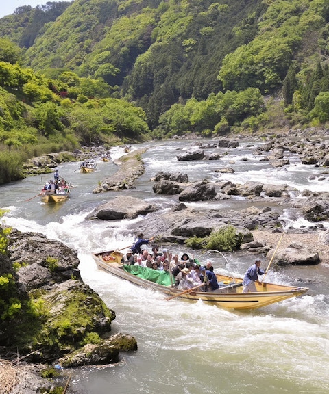 Boat ride on Hozugawa River in Kyoto with cherry blossoms and lush greenery.
