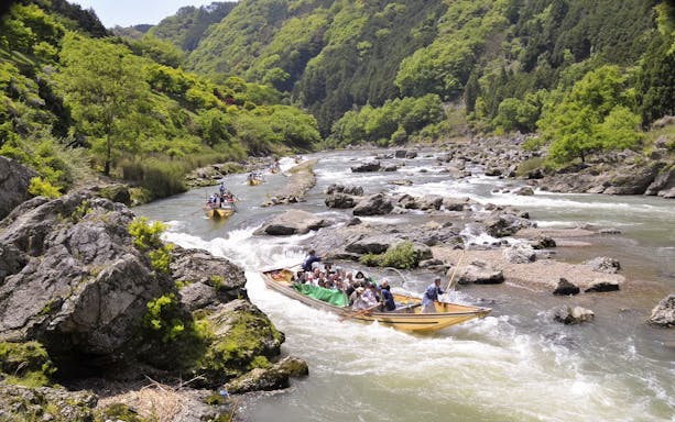 Boat ride on Hozugawa River in Kyoto with cherry blossoms and lush greenery.