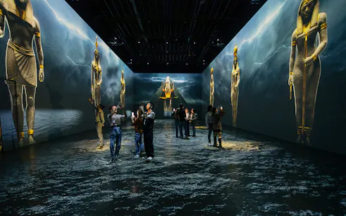 Visitors explore Tutankhamun immersive exhibition with large Egyptian statues projected on walls.