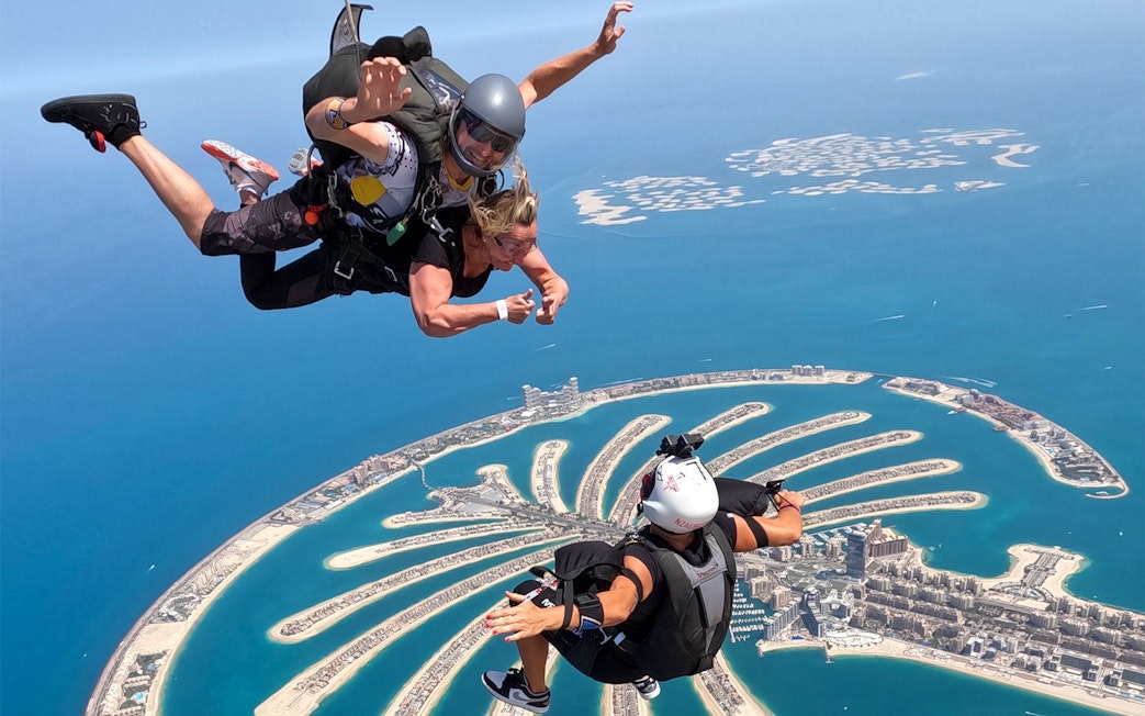 Skydivers tandem jumping over Palm Jumeirah, Dubai with aerial view of islands.