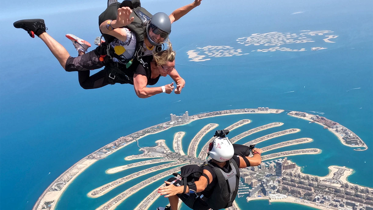 Skydivers tandem jumping over Palm Jumeirah, Dubai with aerial view of islands.