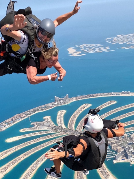 Skydivers tandem jumping over Palm Jumeirah, Dubai with aerial view of islands.