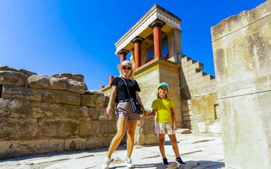 Visitors exploring Knossos Palace ruins in Heraklion, Crete, with iconic red columns.