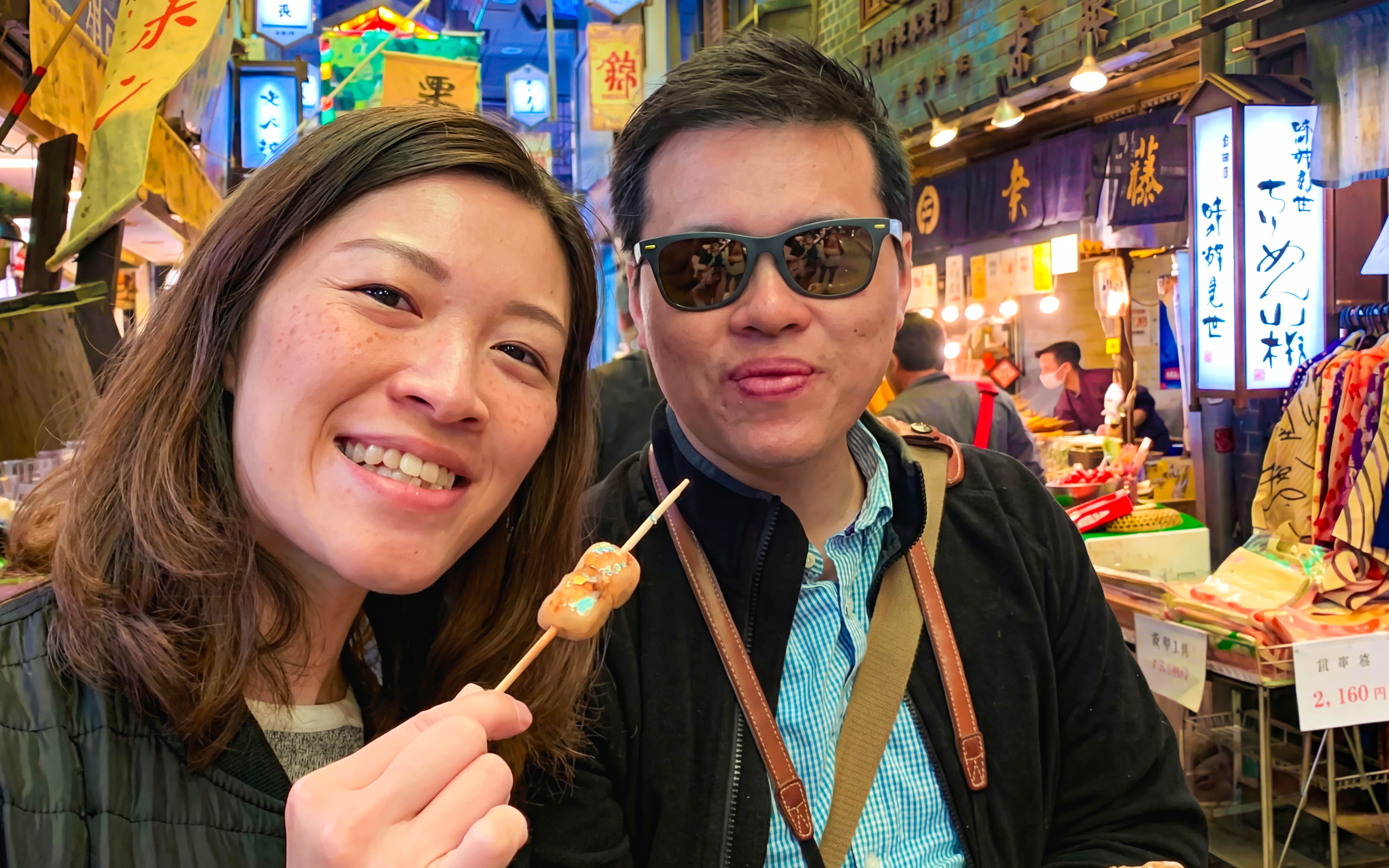 Visitors enjoying skewered snacks at Nishiki Market in Kyoto.