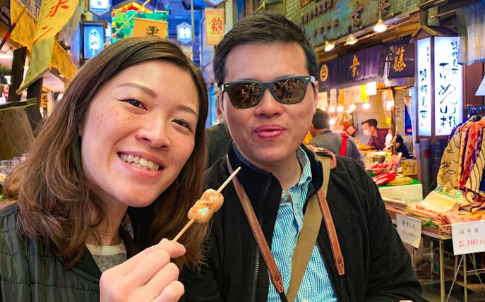 Visitors enjoying skewered snacks at Nishiki Market in Kyoto.