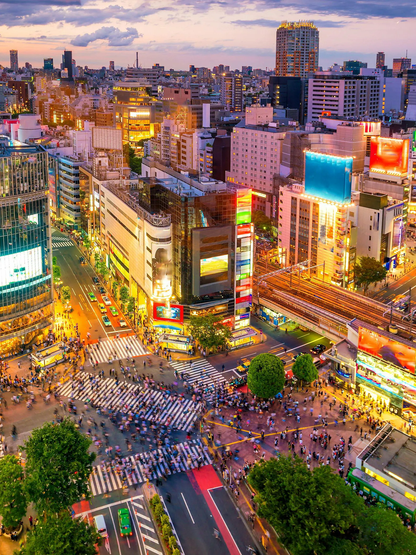 Shibuya Crossing in Tokyo viewed from above, bustling with pedestrians and surrounded by city lights.