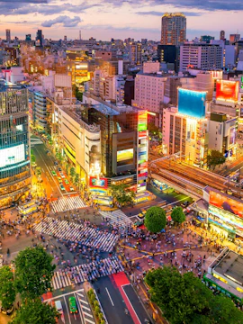 Shibuya Crossing in Tokyo viewed from above, bustling with pedestrians and surrounded by city lights.