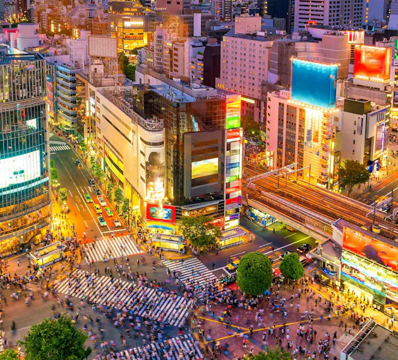 Shibuya Crossing in Tokyo viewed from above, bustling with pedestrians and surrounded by city lights.