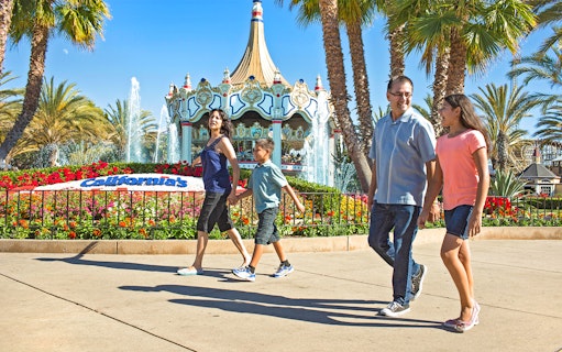 Family walking past the entrance of California's Great America with carousel and fountains.