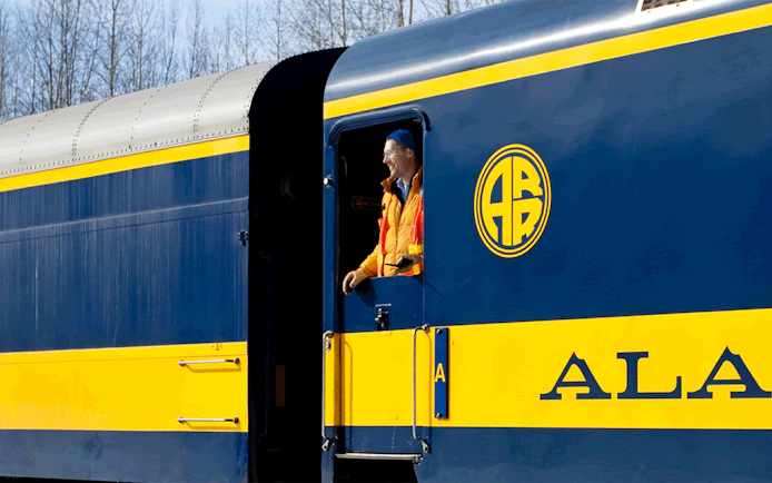 Train conductor on Alaska Railroad engine with logo visible.