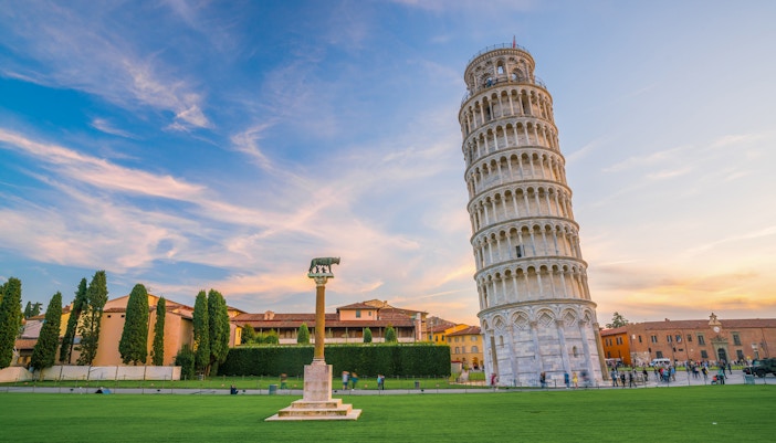 Leaning Tower of Pisa with surrounding lawn and buildings at sunset.
