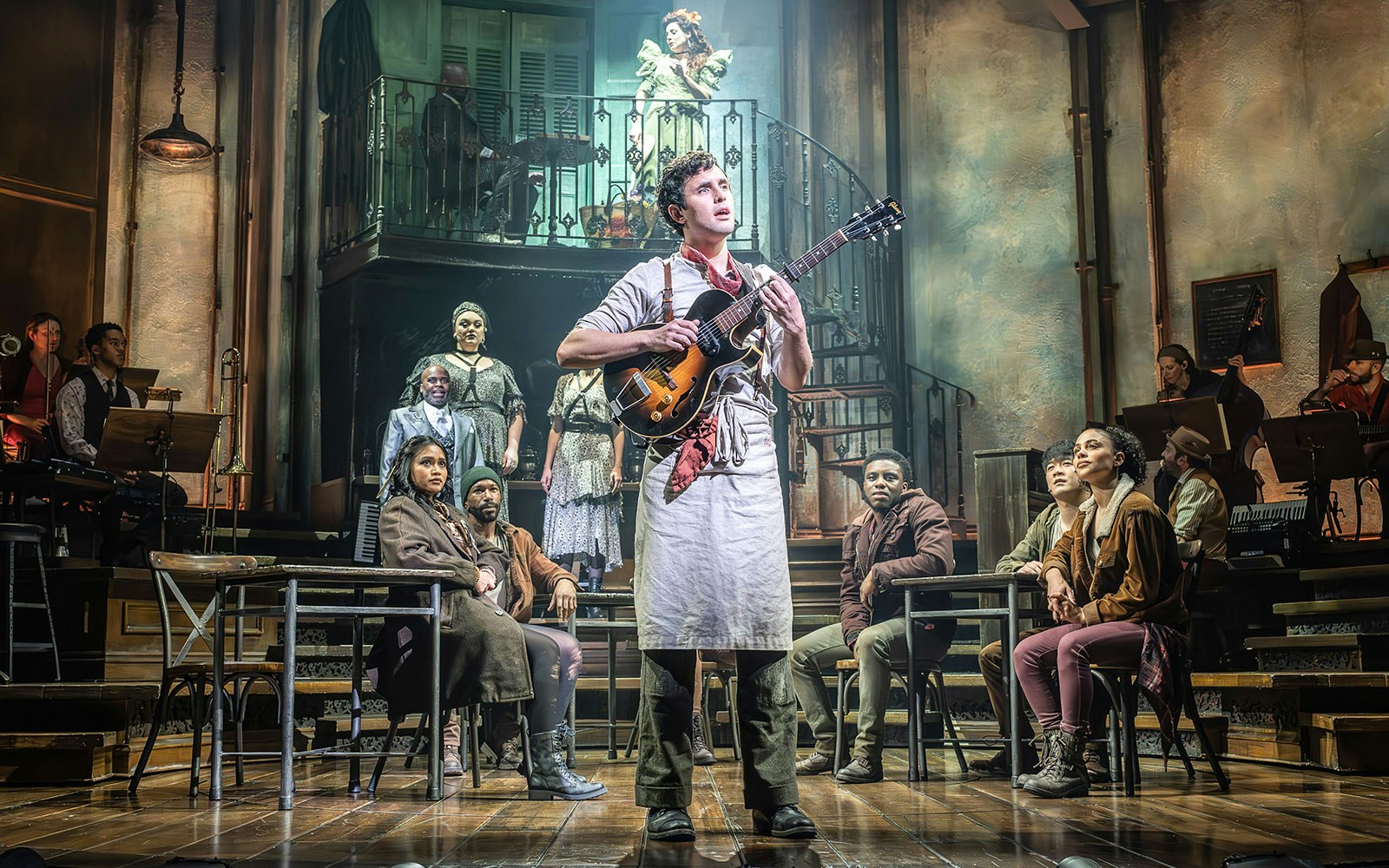 Musician on stage with guitar, surrounded by actors in a theatrical ghost story setting.