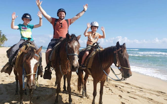 Three people horseback riding on Macao Beach with ocean in the background.