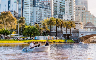 Self-drive boat on Yarra River with cityscape and palm trees in Melbourne.