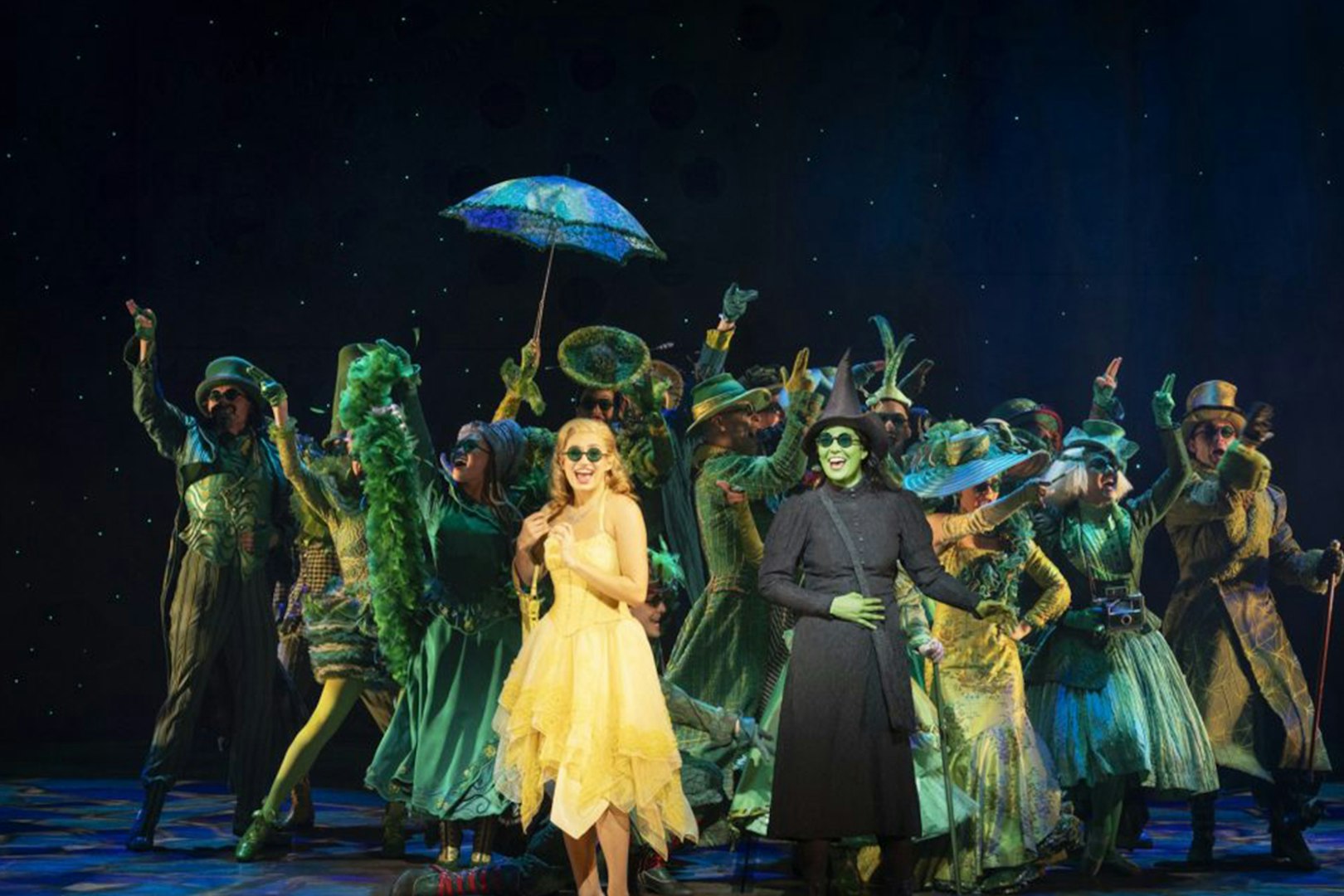 Cast performing in "Wicked" at Lyric Theatre, vibrant costumes and stage setting.