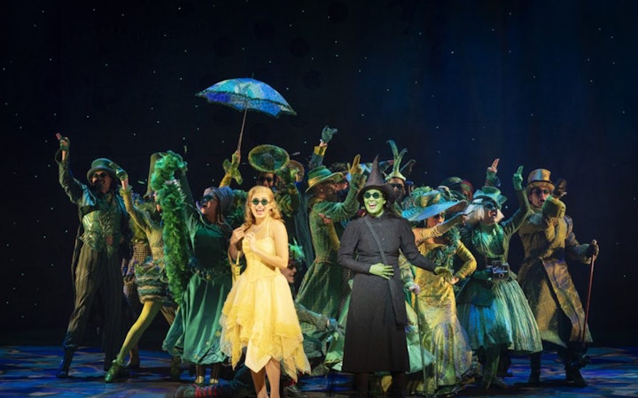 Cast performing in "Wicked" at Lyric Theatre, vibrant costumes and stage setting.
