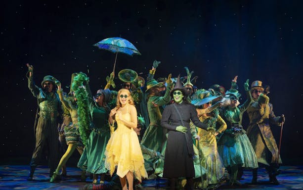Cast performing in "Wicked" at Lyric Theatre, vibrant costumes and stage setting.