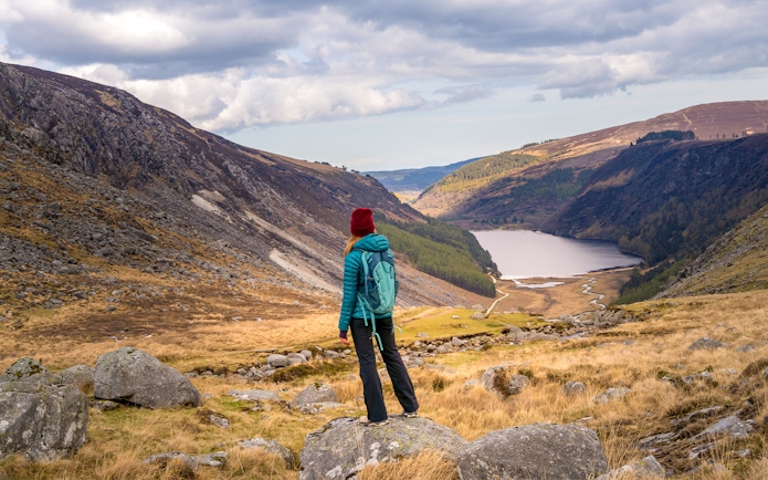 Person hiking in Glendalough National Park, overlooking Wicklow Mountains and lake.