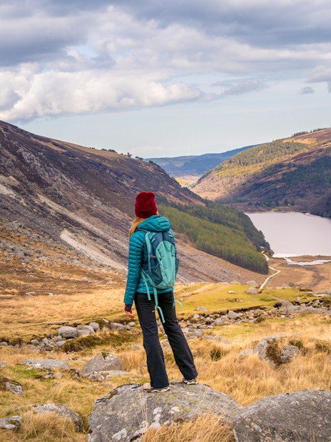 Person hiking in Glendalough National Park, overlooking Wicklow Mountains and lake.