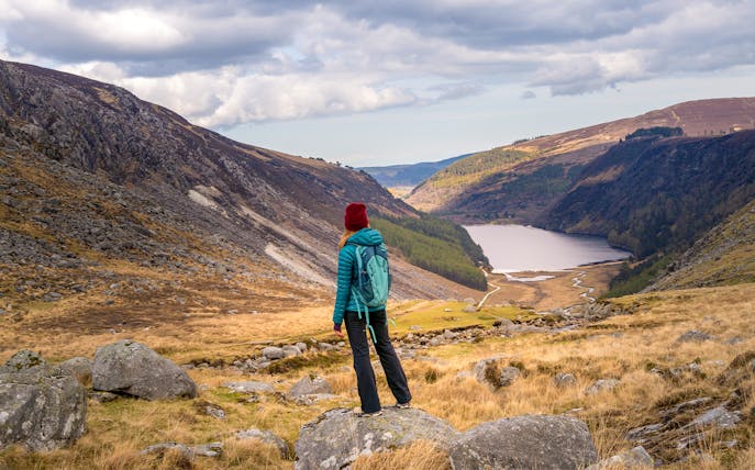 Person hiking in Glendalough National Park, overlooking Wicklow Mountains and lake.