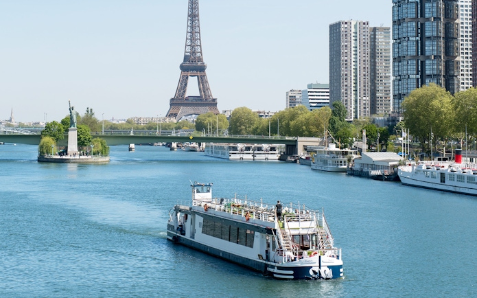THEO boat cruising on the Seine in Paris with Eiffel Tower and Statue of Liberty replica in view.