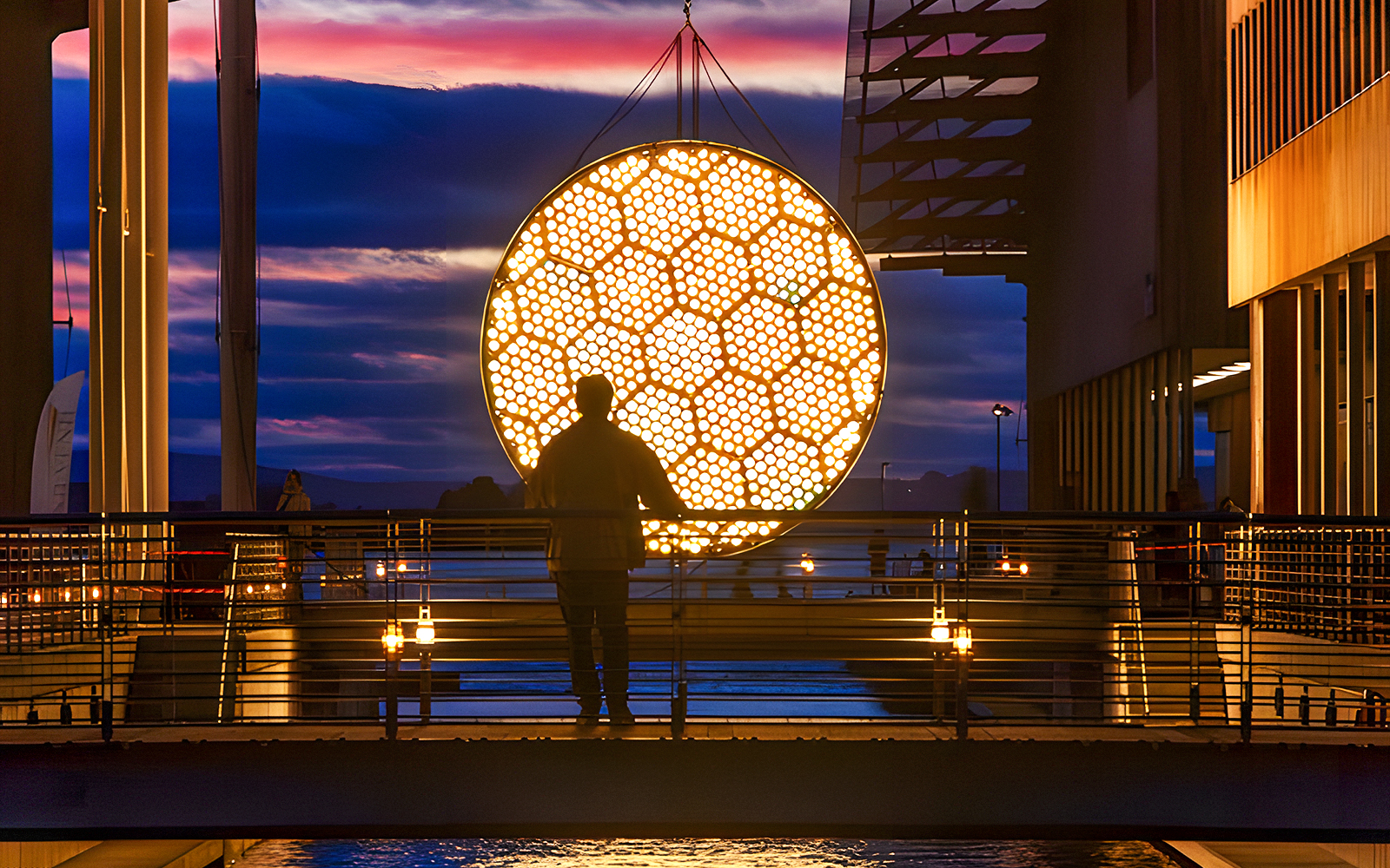Silhouette of a person viewing illuminated art installation during Amsterdam Light Festival canal cruise.