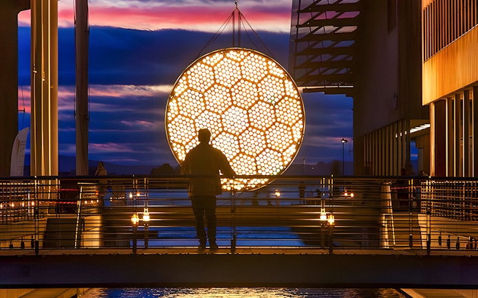 Silhouette of a person viewing illuminated art installation during Amsterdam Light Festival canal cruise.