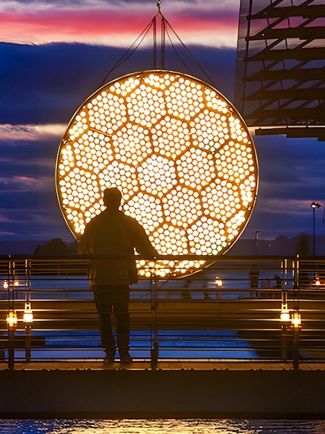Silhouette of a person viewing illuminated art installation during Amsterdam Light Festival canal cruise.