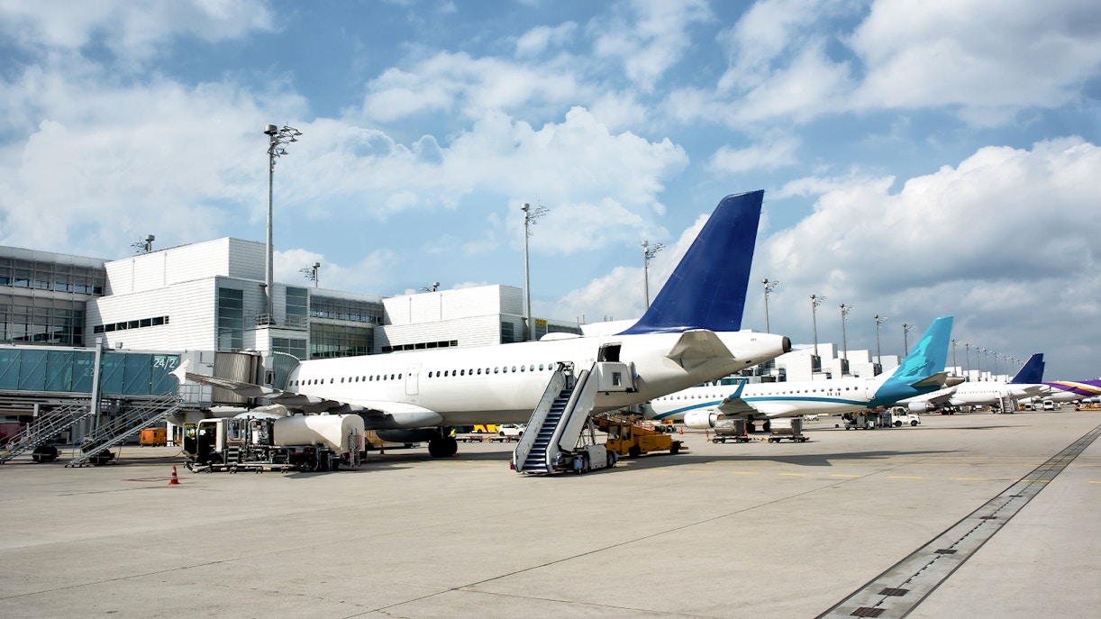 Plane parked on airport runway with boarding stairs and terminal in view.