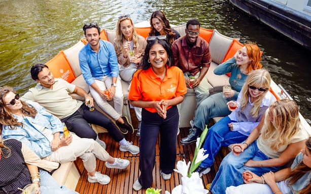 Group enjoying drinks on a luxury open boat cruise in Amsterdam canal.