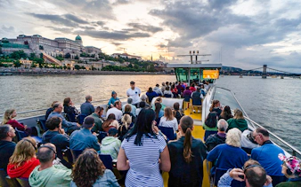 Guests on Budapest Sunset Cruise with view of Buda Castle and Chain Bridge.