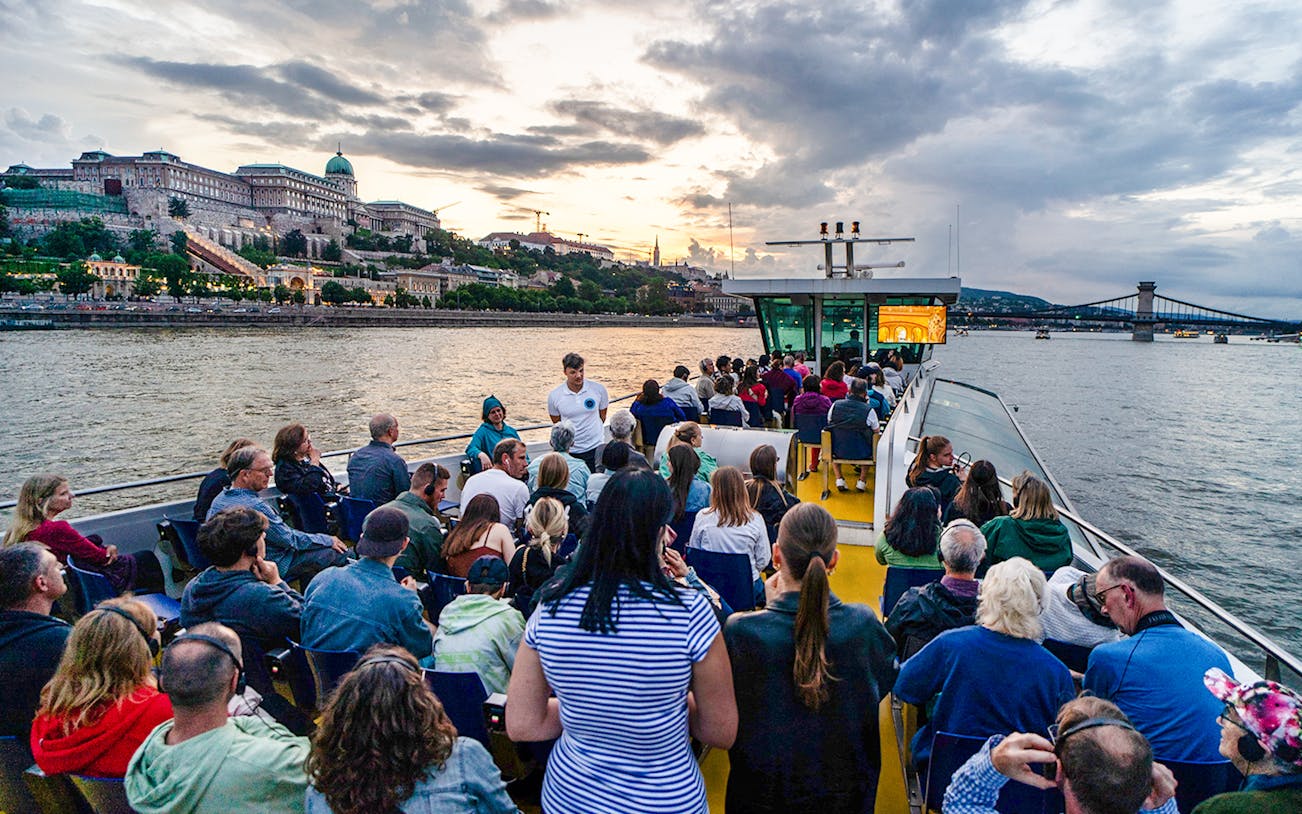 Guests on Budapest Sunset Cruise with view of Buda Castle and Chain Bridge.