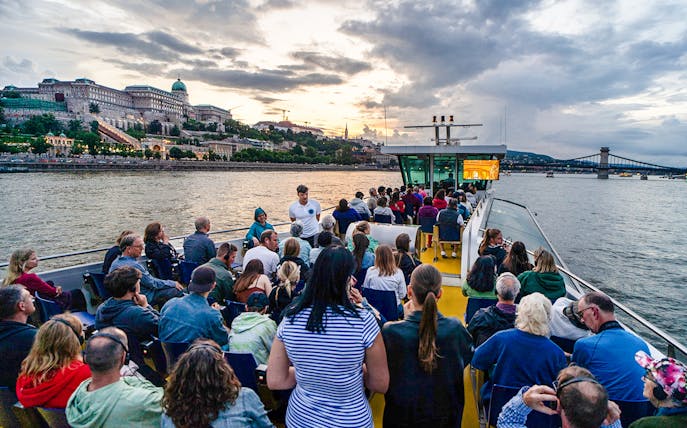 Guests on Budapest Sunset Cruise with view of Buda Castle and Chain Bridge.