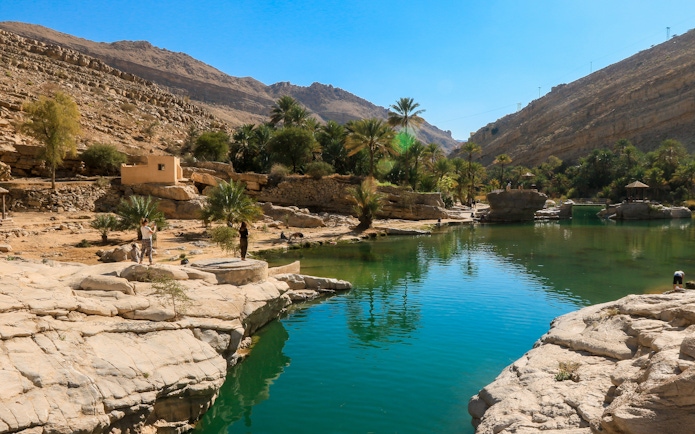 Wadi Shab Oasis in Oman with clear waters, rocky mountains, and lush greenery.