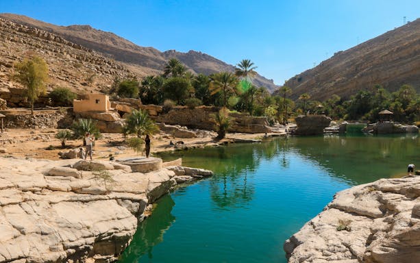 Wadi Shab Oasis in Oman with clear waters, rocky mountains, and lush greenery.