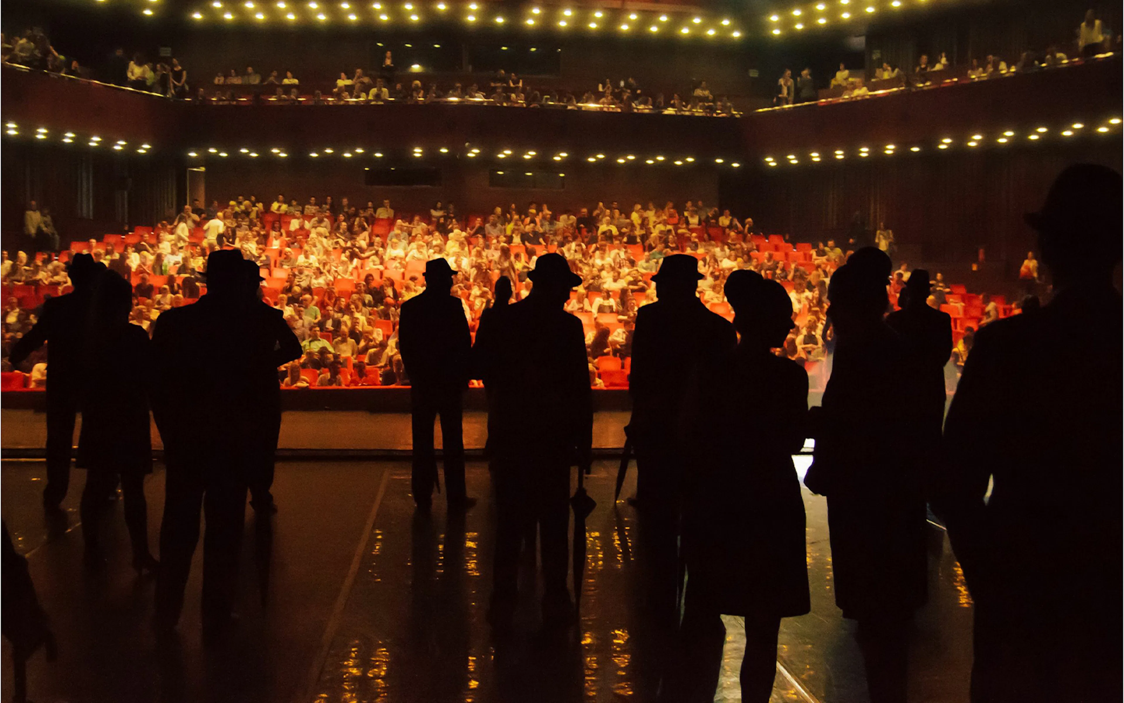 Silhouetted performers on stage facing a full audience in a West End theatre.